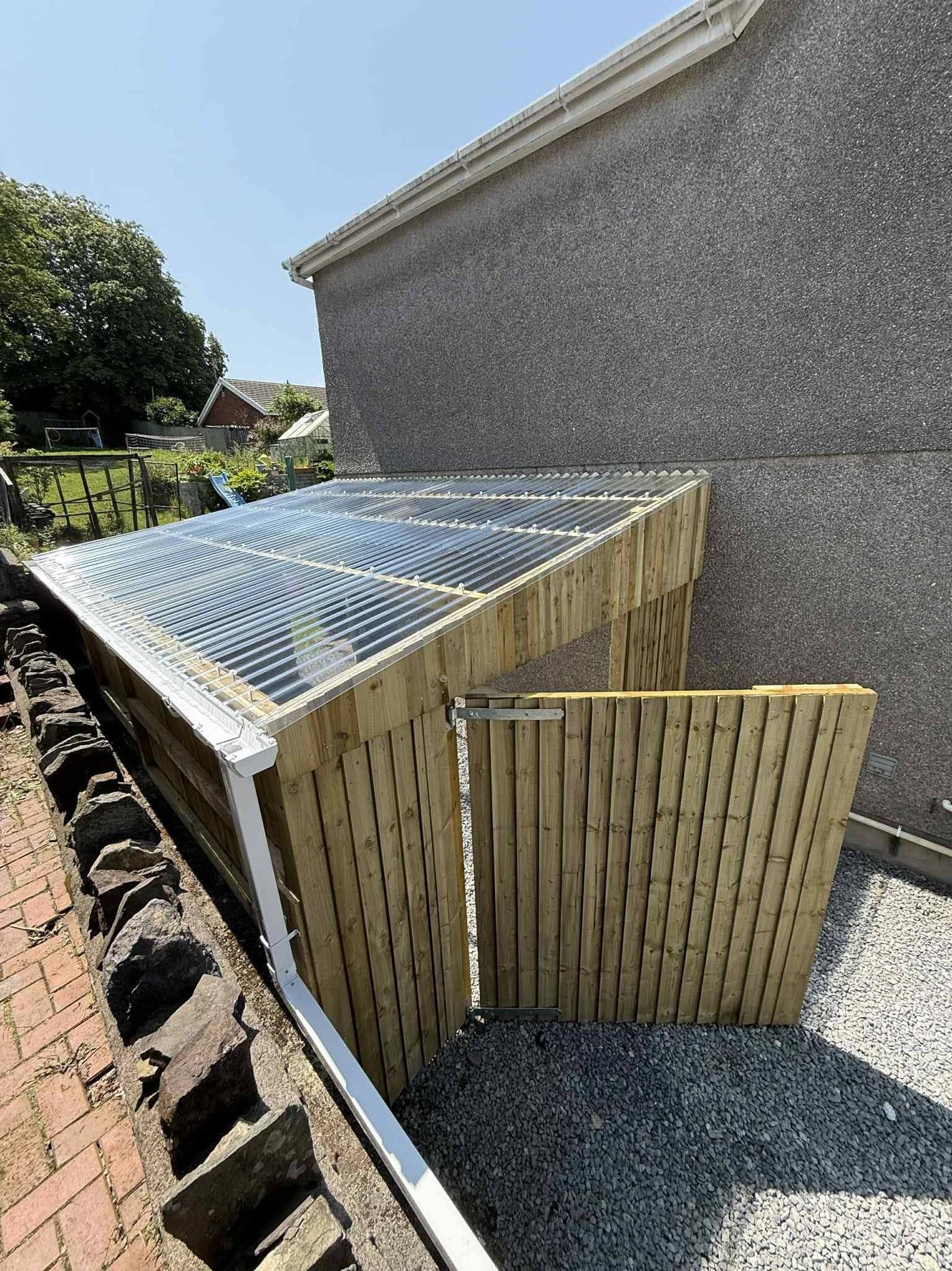 Timber gate and screening beside a house with a clear corrugated roof over the enclosure